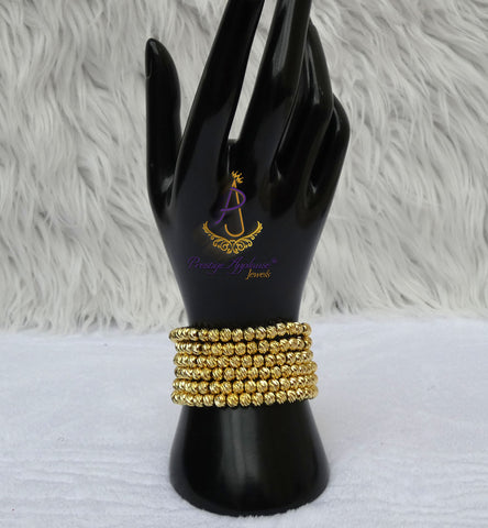 A set of gold beaded multi-strand bracelets displayed on a black hand-shaped jewelry stand against a white faux fur background.