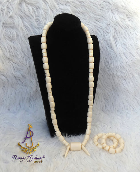 An off-white beaded necklace displayed on a black mannequin bust, with matching beaded bracelets placed beside it on a white faux-fur background. 